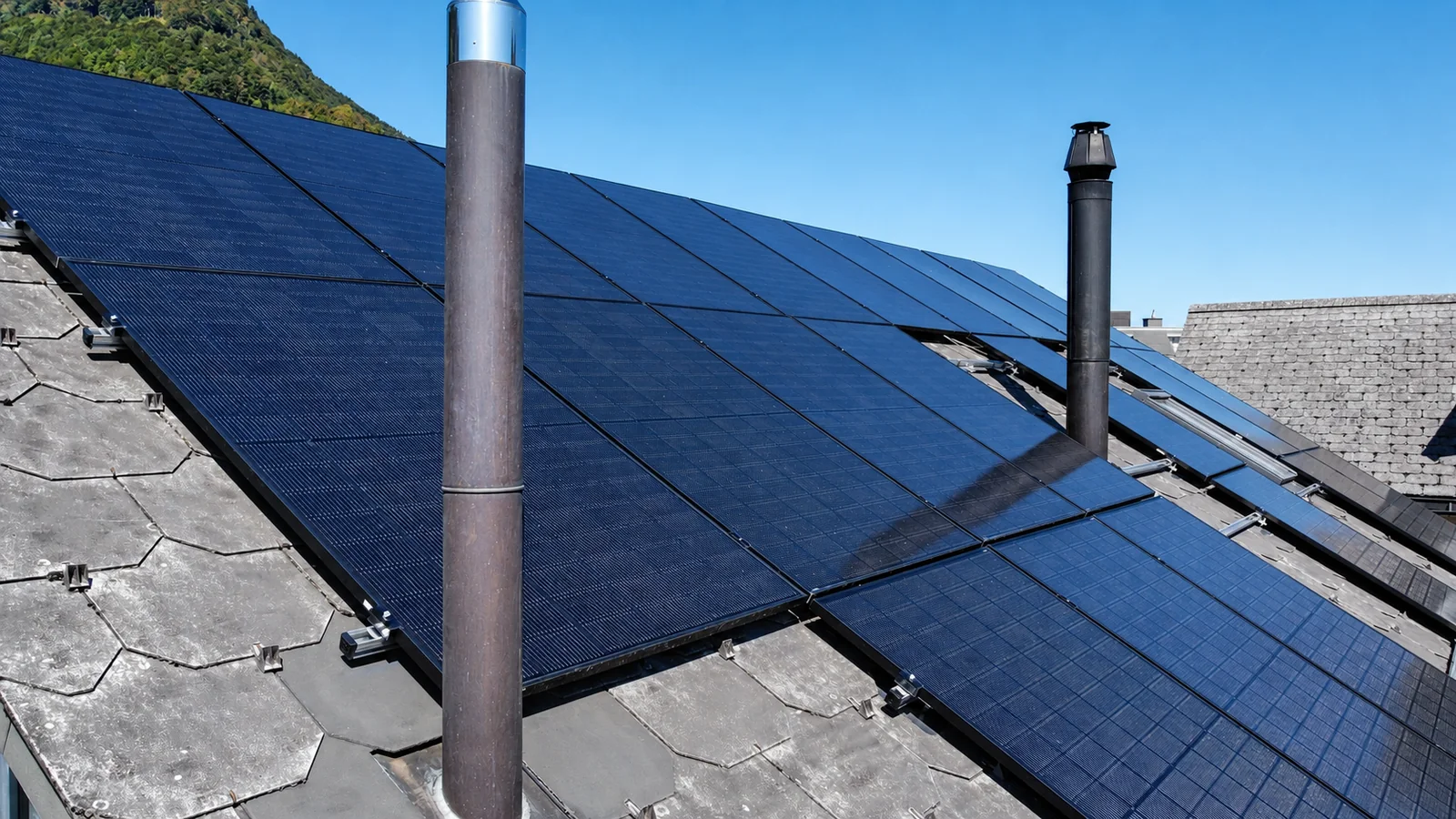 Schwarze Photovoltaikmodule auf einem Schieferdach zwischen zwei Kaminen