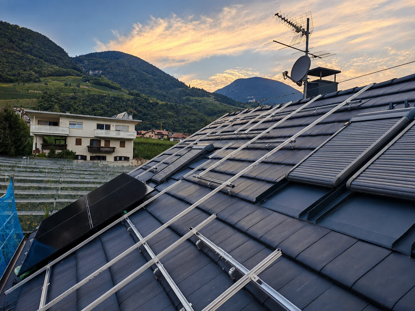 Montageschienen für Photovoltaik auf einem dunklen Ziegeldach im Abendlicht vor Südtiroler Bergen